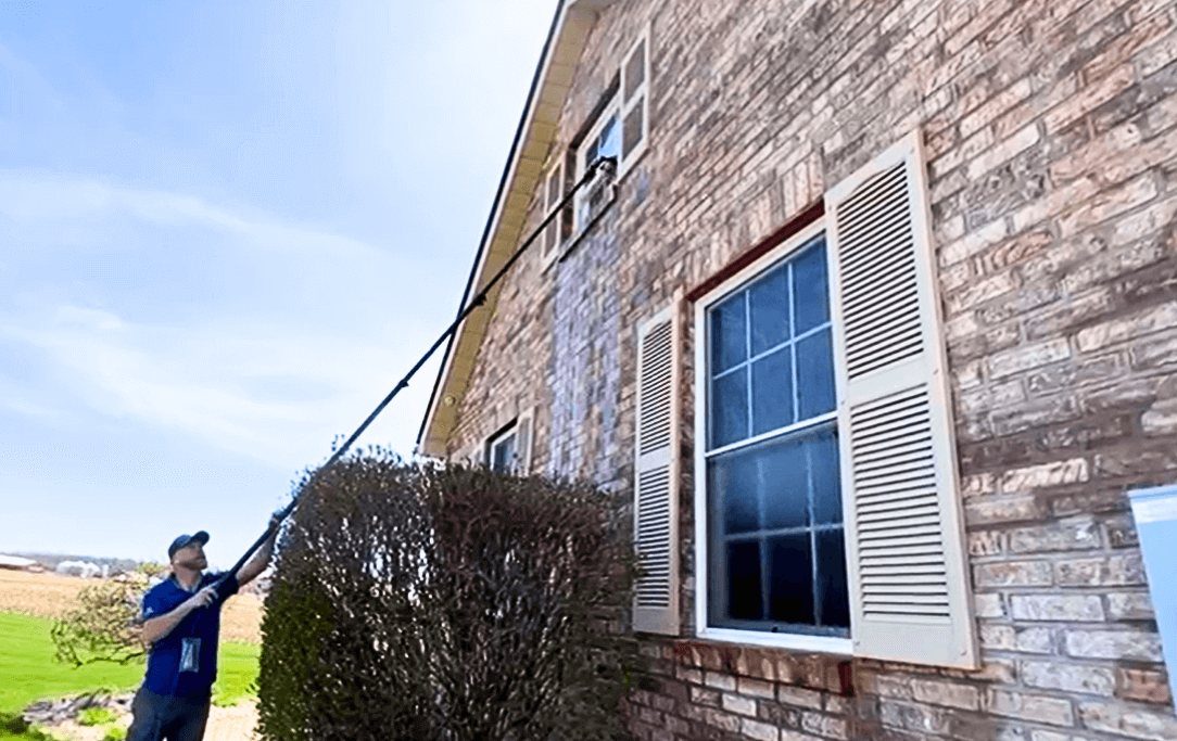 Crew member soft washing the brick front of an Indiana home with an extension wand