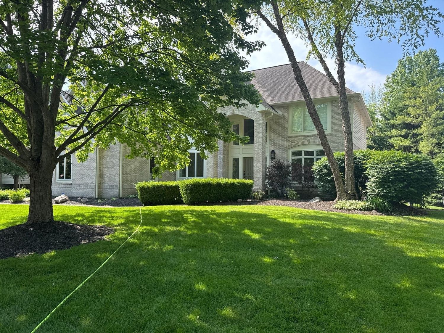 Large Zionsville home behind mature trees and an open lawn after exterior cleaning